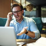 Angry man in glasses on phone, yelling in front of computer