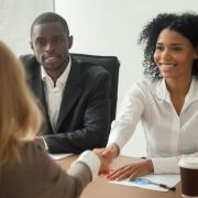 Work colleagues in meeting, two women shaking hands with man sitting at table