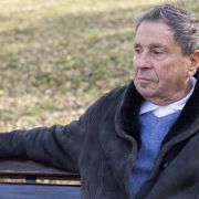 Pensive older man sitting on park bench looking away