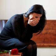 Woman in black dress, crying in church pew with rose; she is grieving a death