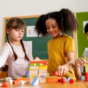 Three children playing with wooden blocks in classroom