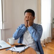 Man sitting at his desk suffering from brain fog, rubbing his eyes