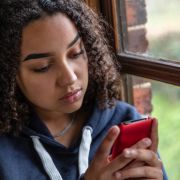 sad teen girl looking at social media on red smartphone