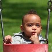 Latin African American Baby in Swing with Finger in his mouth Looking