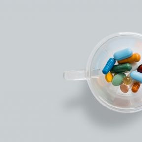 transparent coffee cup with colourful pills on gray background. 