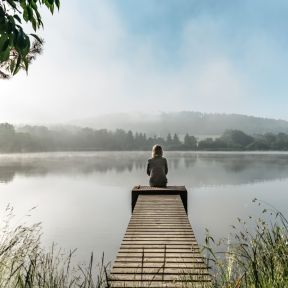 Woman sitting alone at far end of dock on lake