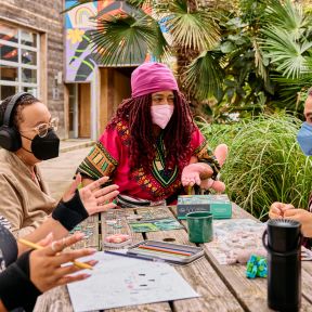 Four masked people sit at a table outdoors, chatting..