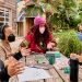 Four masked people sit at a table outdoors, chatting..