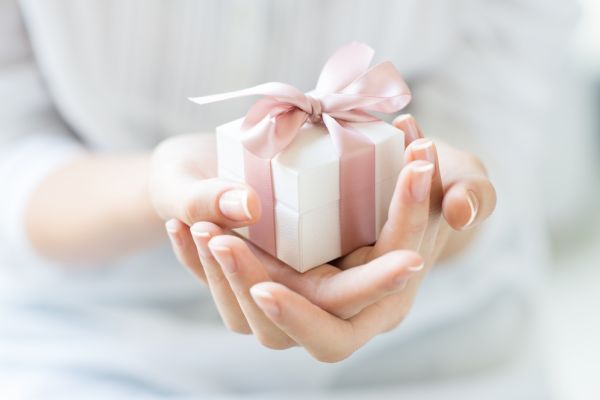 Female hands holding a small gift wrapped with pink ribbon.