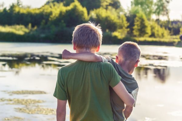 Two young brothers standing in front for a pond.