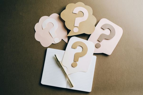 An open notebook with a pen and paper questionmarks