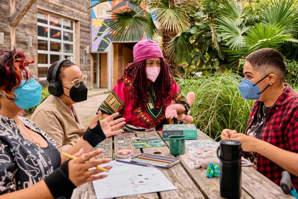 Four masked people sit at a table outdoors, chatting..